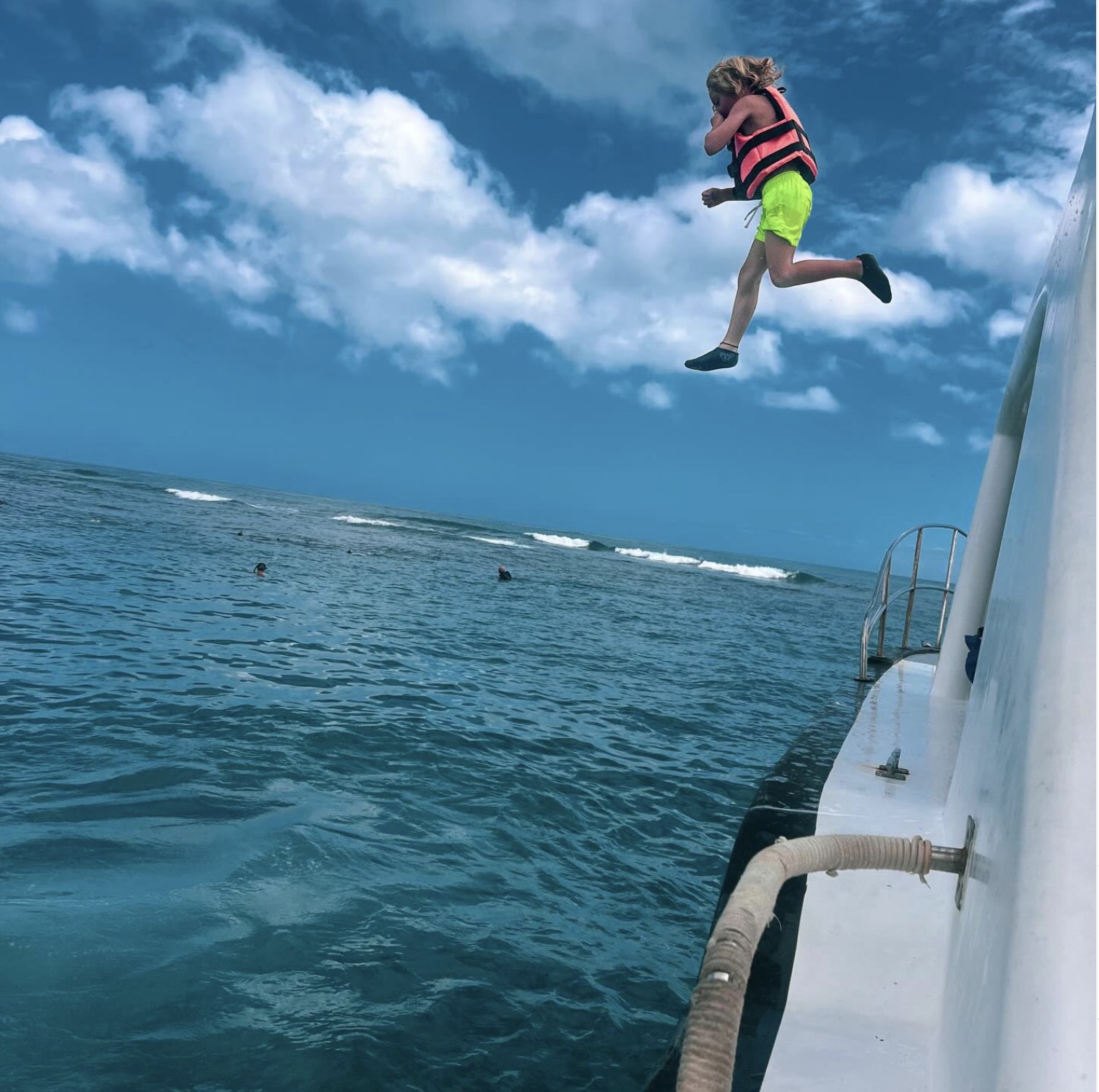 A child jumping into the sea from the boat wearing a life jacket.