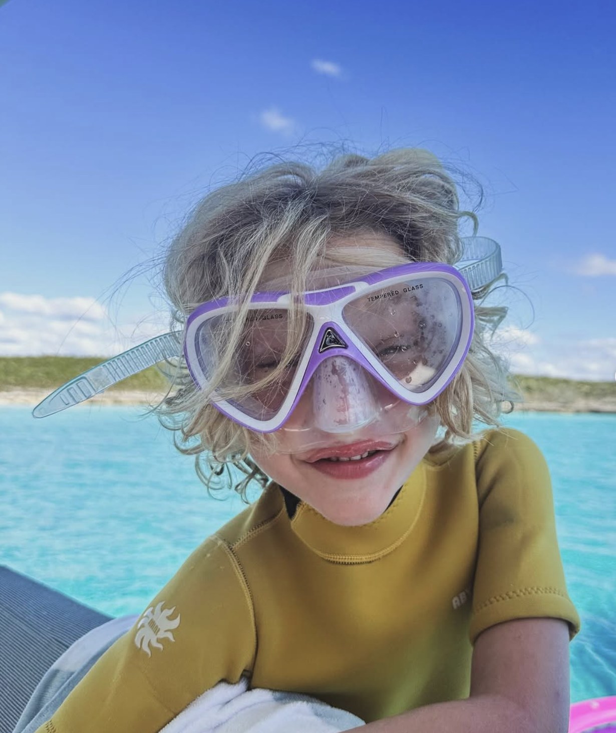 A child wearing a snorkel mask above clear blue water.