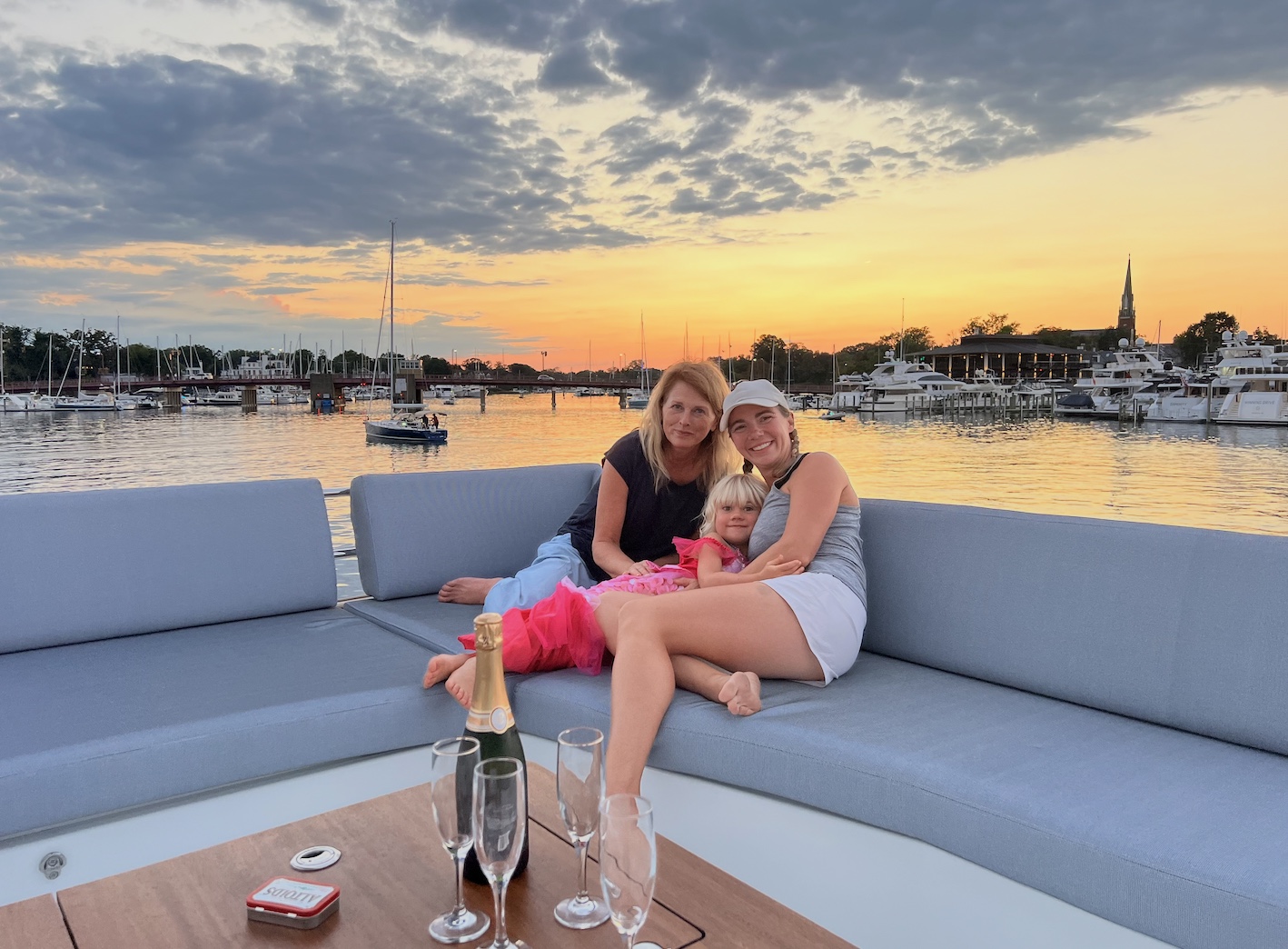 Three people relaxing together aboard a boat at sunset in a marina.