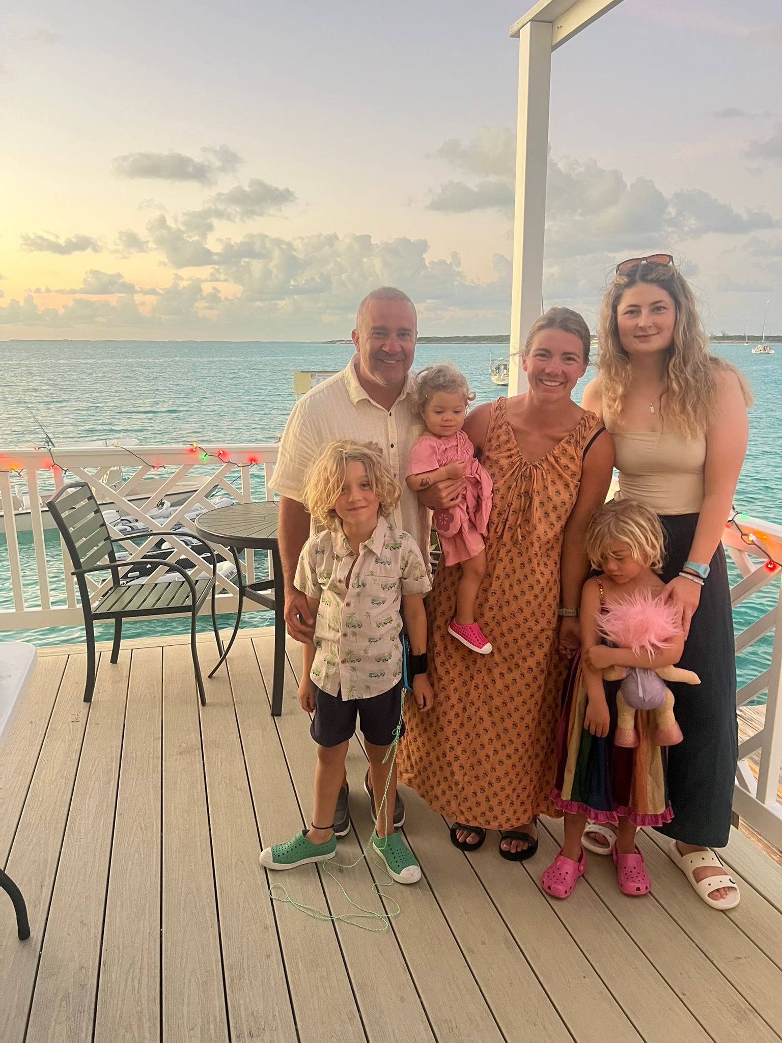 A group of adults and children standing together on a waterfront deck at sunset.