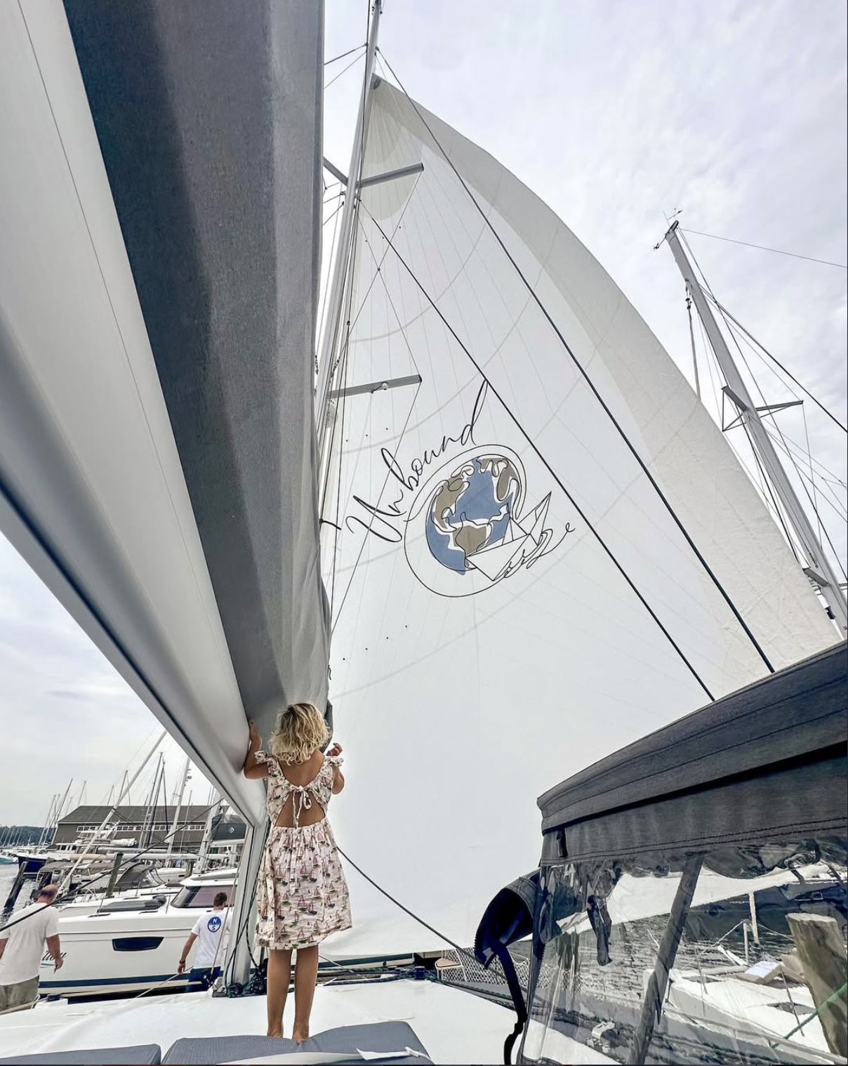 Child standing beneath SV Unbound’s sail, which carries the boat’s mark.